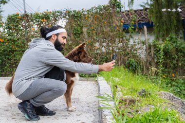 Çiçekler ve yeşilliklerle çevrili bahçe yolunda akıllı telefona bakan insan ve köpek.