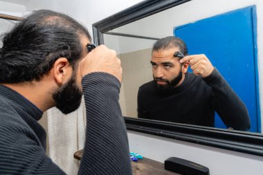 Sakallı Kolombiyalı adam saç dökülme tedavisinin bir parçası olarak kafa derisinde mikronedle rulo kullanıyor.