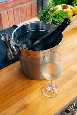 Şarap şişesi buz kovasında soğutuluyor, otlar ve meyveler ahşap yüzeyde.