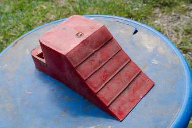 Kırmızı plastik tekerlek tıkanması mavi varil kapağına yerleştirilmiş ve arka planda çimenler var.