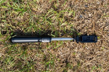 Teleskopik kollu siyah ve gümüş selfie çubuğu kuru çimenlere konur.