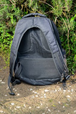 Yeşil yapraklı ve taşlı toprak yola yerleştirilmiş ağlı siyah sırt çantası