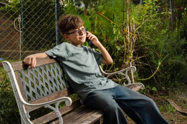 Bahçedeki dekoratif bankta oturmuş telefonla konuşan genç adam..