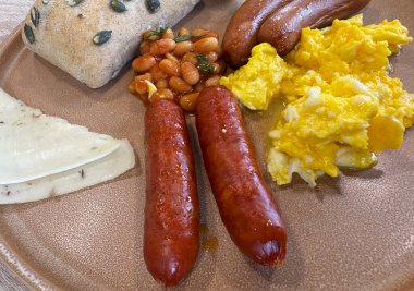 Kahvaltı tabağının genel manzarası. Izgara sosis, peynir, soslu fasulye ve kızarmış yumurta..