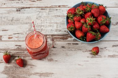 Taze meyve suyu, sallamak, bir mason kavanoza bir saman ile çilek milkshake. Geniş mavi kapta sulu olgun organik taze çilek yığını. Işık rustik ahşap arka plan