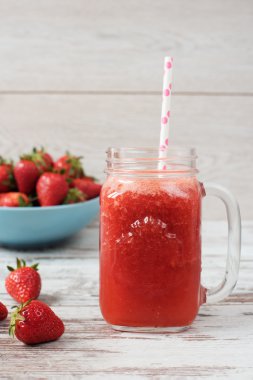 Taze meyve suyu, sallamak, bir mason kavanoza bir saman ile çilek milkshake. Geniş mavi kapta sulu olgun organik taze çilek yığını. Işık rustik ahşap arka plan