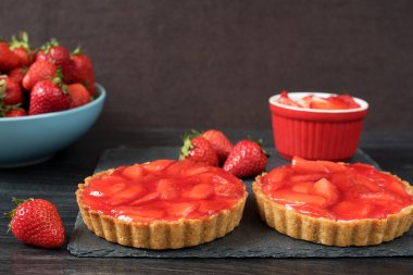 Çikolatalı tart, beyaz çikolata ve mascarpone krema, ile tartalette üstte taze çilek. Büyük mavi kase çilek tam. Siyah ahşap arka plan.