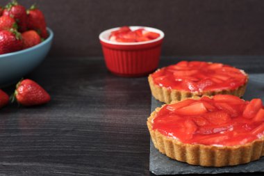 Çikolatalı tart, beyaz çikolata ve mascarpone krema, ile tartalette üstte taze çilek. Büyük mavi kase çilek tam. Siyah ahşap arka plan