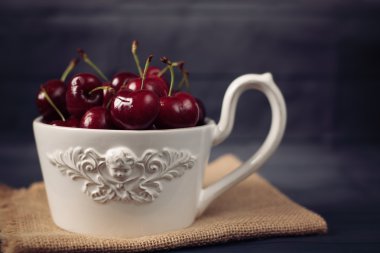 Büyük bir fincan kahve açık melek, beyaz kase taze kiraz ile tam meyve. Rustik koyu arka plan, shabby chic, vintage renklendirme