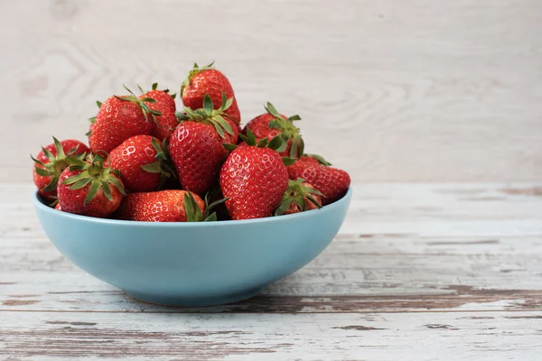 Pile of juicy ripe organic fresh strawberries in a large blue bowl. Light rustic wooden background — Stock Photo, Image
