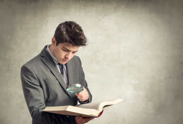 Joven hombre de negocios mirando un libro con lupa —  Fotos de Stock