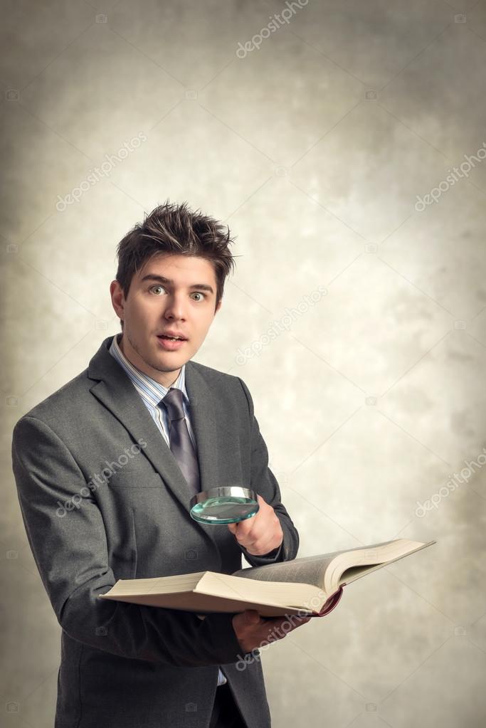 Young businessman looking at a book with magnifying glass