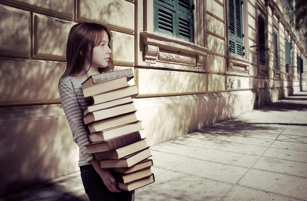 Pequena menina cuidar pilha de livros — Fotografia de Stock