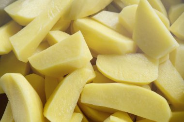 Üst manzara, dilimlenmiş taze patatesleri bıçakla, arka planda pişirme malzemesi olan parçalara ayırır.