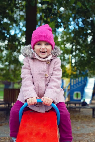Pembe ceketli ve örgü şapkalı küçük sarışın kız çocuk parkında salıncakta sallanıyor. Dört yaşındaki kız gülüyor. Soğuk mevsimde sonbahar parkında eğlence. Mutlu bir çocukluk dönemi hariç.