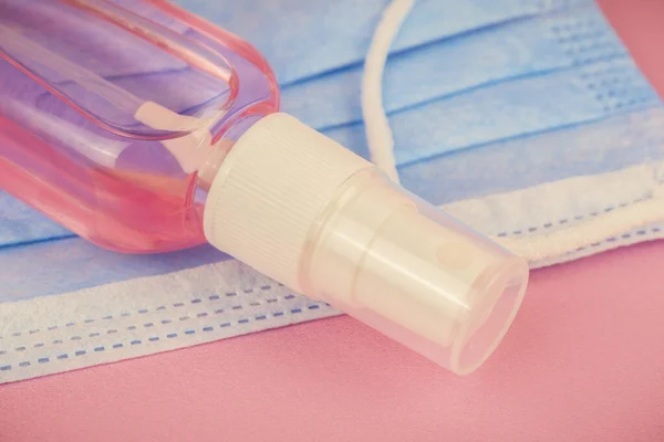 Dezenfeksiyon için antiseptik spreyi kapatın. Pembe arka planda mavi misk kokulu el dezenfektanı şişesi. Tıp ve kozmetoloji teması.