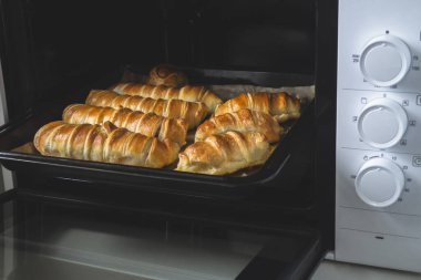 Hamurdaki sosisler fırın tepsisinde. Koyu renkli parşömen üzerinde pişirme, yaşam tarzı. Evde fırında pişirme.