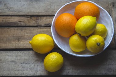 Limonlar ve portakallar ahşap bir arka planda beyaz bir kasede