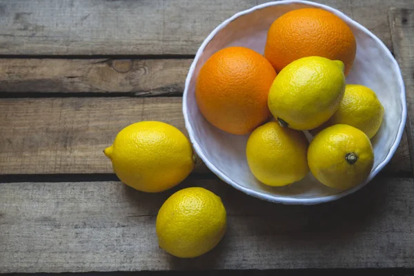 Limonlar ve portakallar ahşap bir arka planda beyaz bir kasede