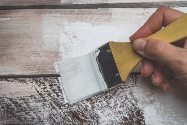 Kadının eli bir boya fırçası tutuyor ve tahta bir tahtayı beyaza boyuyor. Onarım ve inşaat kavramı