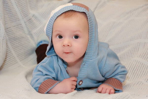 cute baby in the sweater with the hood lying on his stomach on a blue blanket