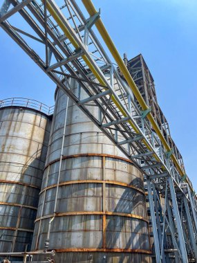 The viewpoint showcases extensive industrial storage tanks and robust steel frameworks beneath a clear blue sky