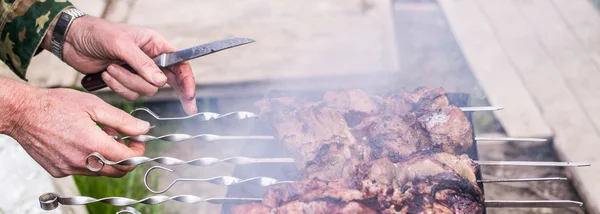 Man with knife in hand is cooking barbecue, only hands. Delicious grilled meat on grill. Barbecue weekend. Selective focus — Stock Photo, Image