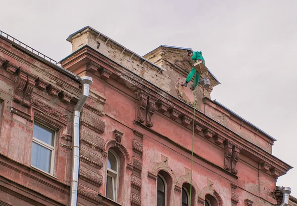 Builder lezec visí na vrcholu průčelí budovy mluvící mobilní telefon Stock Snímky