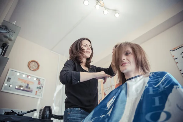 Close-up van de hand van kapper maken van kapsel voor blonde vrouw. Stockafbeelding