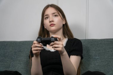 Elinde kumandayla oturma odasındaki rahat bir koltukta oturup oyun oynayan genç bir kız boş zamanlarının tadını çıkarıyor.