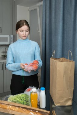 Masada kağıt poşetin yanında taze domatesler tutan genç bir kız, sürdürülebilir alışveriş uygulamalarını destekliyor ve plastik kullanımını azaltıyor. Dikey fotoğraf
