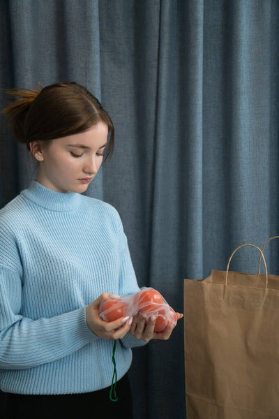 Young girl holding fresh tomatoes in a reusable mesh bag next to a paper bag, promoting sustainable shopping practices and reducing plastic use. Vertical photo