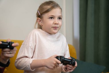 Genç kız elinde bir oyun kumandası tutarken yoğun bir şekilde ekrana odaklanmış, evde oyun oynamanın keyfini çıkarıyor- gündelik, mutlu, dijital oyun ve eğlenceye dalmış