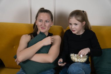 Anne ve kızı oturma odalarındaki sarı bir kanepede gevşeyip patlamış mısır yiyip uzaktan kumanda tutarak sıradan bir film gecesinin tadını çıkarıyorlar.