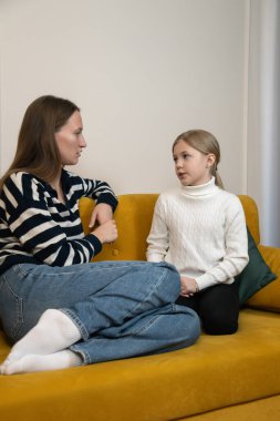 Sarı bir kanepede oturan kadın ve genç kız ciddi ve anlamlı bir anne-kız sohbeti yaparken birbirlerini dinliyorlar iletişim ve bağ kurmaya odaklanıyorlar. Dikey fotoğraf