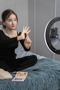 Genç bir güzellik blogcusu, akıllı telefon ve zil ışığı kullanarak çevrimiçi seyircisine makyaj dersi verirken fırçayla allık sürüyor.
