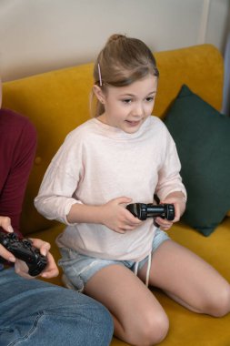 Genç kız elinde bir oyun kumandası tutarken yoğun bir şekilde ekrana odaklanmış, evde oyun oynamanın keyfini çıkarıyor- gündelik, mutlu, dijital oyun ve eğlenceye dalmış. Dikey fotoğraf