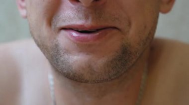 Tıraşsız, sakallı, dudaklarını ve çenesini hareket ettiren, dişlerini ve dilini sürekli doğal bir konuşmada gösteren bir adamın aşırı yakın çekimi.