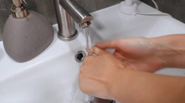 Temizliği korumak ve Coronavirus gibi mikropların, bakterilerin ve virüslerin sağlığa yayılmasını önlemek için beyaz seramik lavaboda sabun ve akan suyla nazikçe el yıkama.