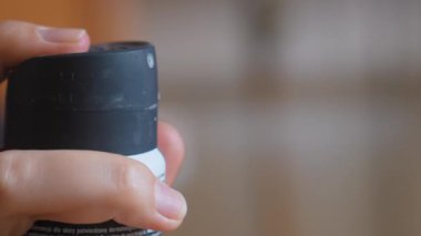 Deodorant spreyini serbest bırakmak için spreyin başlığına bastıran ve odak için bulanık bir arka planla günlük hijyen rutinini gösteren bir kadın elinin yakın plan çekimi.