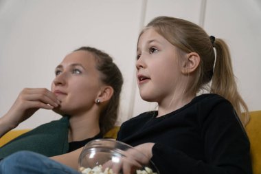 Anne ve kızı rahat bir film gecesinde kaynaşıyor, kanepede birlikte oturuyor, eğlence için televizyon izlerken bir kaseden patlamış mısır yiyor.