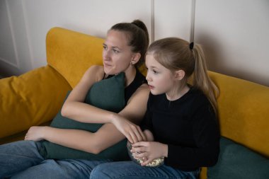 Anne ve kızı rahat bir film gecesinde kaynaşıyor, kanepede birlikte oturuyor, eğlence için televizyon izlerken bir kaseden patlamış mısır yiyorlar. Dikey fotoğraf