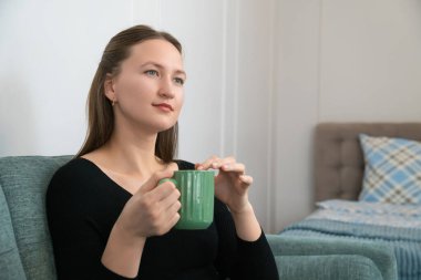 Genç bir kadın rahat bir şekilde kanepede oturur, sıcak bir fincan bitki çayıyla huzurlu bir anın tadını çıkarır, rahat ve huzurlu bir atmosfer yaratır.