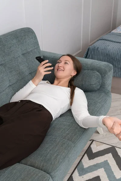 Genç kadın rahat bir şekilde kanepede uzanıyor, akıllı telefonunu kullanıyor, evde boş zamanlarının tadını çıkaran bir sesli mesaj kaydediyor, günlük rutinine ara veriyor. Dikey fotoğraf