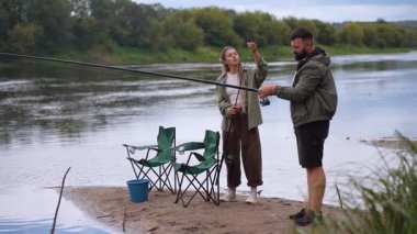 Milenyum çifti, sakallı adamın sevgilisine kumlu bir nehir kıyısında dururken olta ve makarayı nasıl kullanacağını öğretmesiyle birlikte dışarıda kaliteli zaman geçiriyor.