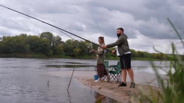 Kafkasyalı genç bir adam ve kadın boş zamanlarını bulutlu bir günde kumlu bir nehir kıyısındaki çubuklarla birlikte avlanarak dışarıda hobilerinin tadını çıkararak ve doğada dinlenerek geçiriyorlar.
