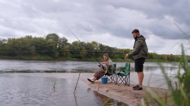 Kafkasyalı genç bir adam ve kadın boş zamanlarını bulutlu bir günde kumlu bir nehir kıyısındaki çubuklarla birlikte avlanarak dışarıda hobilerinin tadını çıkararak ve doğada dinlenerek geçiriyorlar.