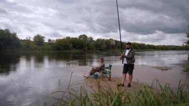 Mutlu genç çift bulutlu bir günde kumlu nehir kıyısında birlikte balık tutarak vakit geçiriyorlar. Romantik açık hava aktiviteleri ve doğayla bağlantı kurmak için ortak bir hobi.