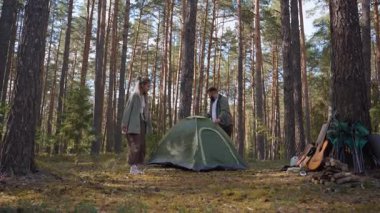 Genç bir adam ve kadın, yeşil kubbe çadırlarını güneşli bir çam ormanında toplamak için birlikte çalışıyorlar. Güzel bir yaz gününde kamp alanlarını açık hava macerasına hazırlıyorlar.
