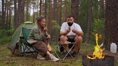 Romantik genç çift kamp alanlarında birlikte yemek yiyor, çam ormanlarında şenlik ateşinde ızgara et ve ekmek yiyorlar, huzurlu bir hafta sonu kaçamağı sırasında, doğayı kucaklıyor ve rahatlatıyorlar.